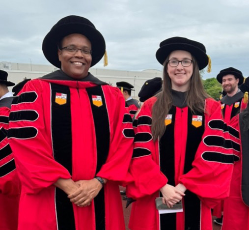 Two students pose in their Ph.D. commencement regalia