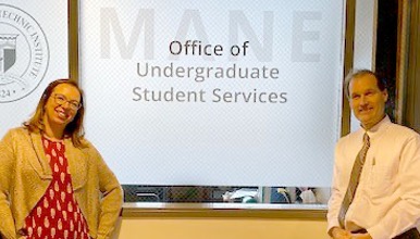 Two advising staff pose in front of office sign