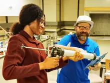 Student works with a professor who holds a piece of equipment